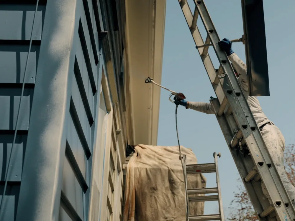 Exterior house painting with spray application on upper siding using ladder access