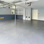 A wide view of a residential interior showing a gray garage floor epoxy finish and custom blue and gray wall painting.