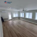 Large room with a fresh interior painting and flooring update, featuring bright windows and neutral wood planks.