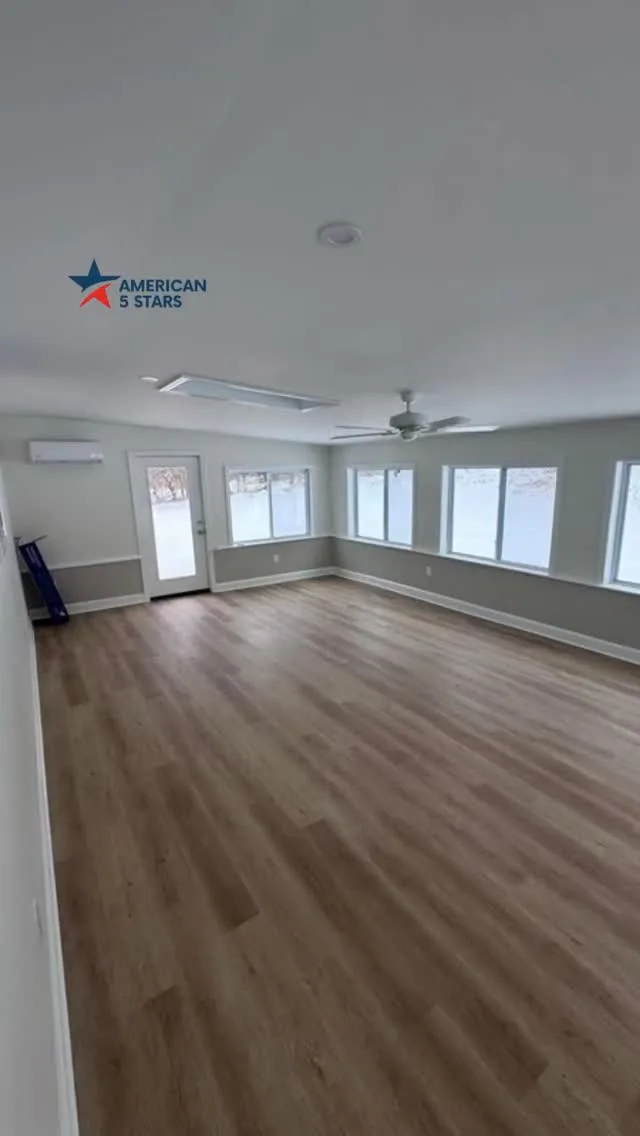 Large room with a fresh interior painting and flooring update, featuring bright windows and neutral wood planks.