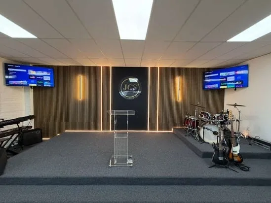 Completed view of the renovated JCS stage, highlighting the central section of custom slat wall panels with integrated LED lighting and pro-AV equipment.